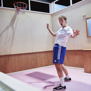Een jongen in sportkleding. Hij staat onder een basketbalring. 