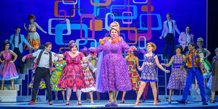 Hairspray Het grote ensemble van Hairspray, dansend in vrolijke jaren 60 kleding. Middenvoor staat Richard Groenendijk als moeder Edna in een enorme paarse jurk.