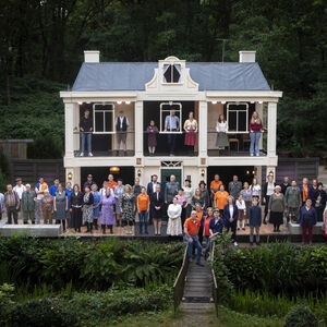 Een grote groep vrolijk met vlaggetjes zwaaiende dansende mensen voor een huis waarop wordt geprojecteerd het beeld van de bevrijding.