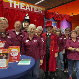 Op de Oogbeurs poseren 10 Komt het Zien medewerkers en vrijwilligers in de gezellige rood pluchen theaterstand.