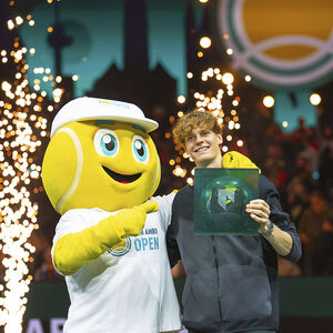 Een tennisser met zijn glazen trofee poseert met de mascotte van het ABN AMRO open