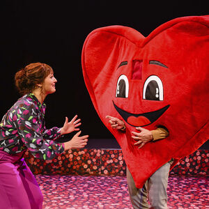 Brigitte Heitzer als Jenny is in gesprek met een groot rood hart. Het hart heeft een grote glimlach en twee handjes.  